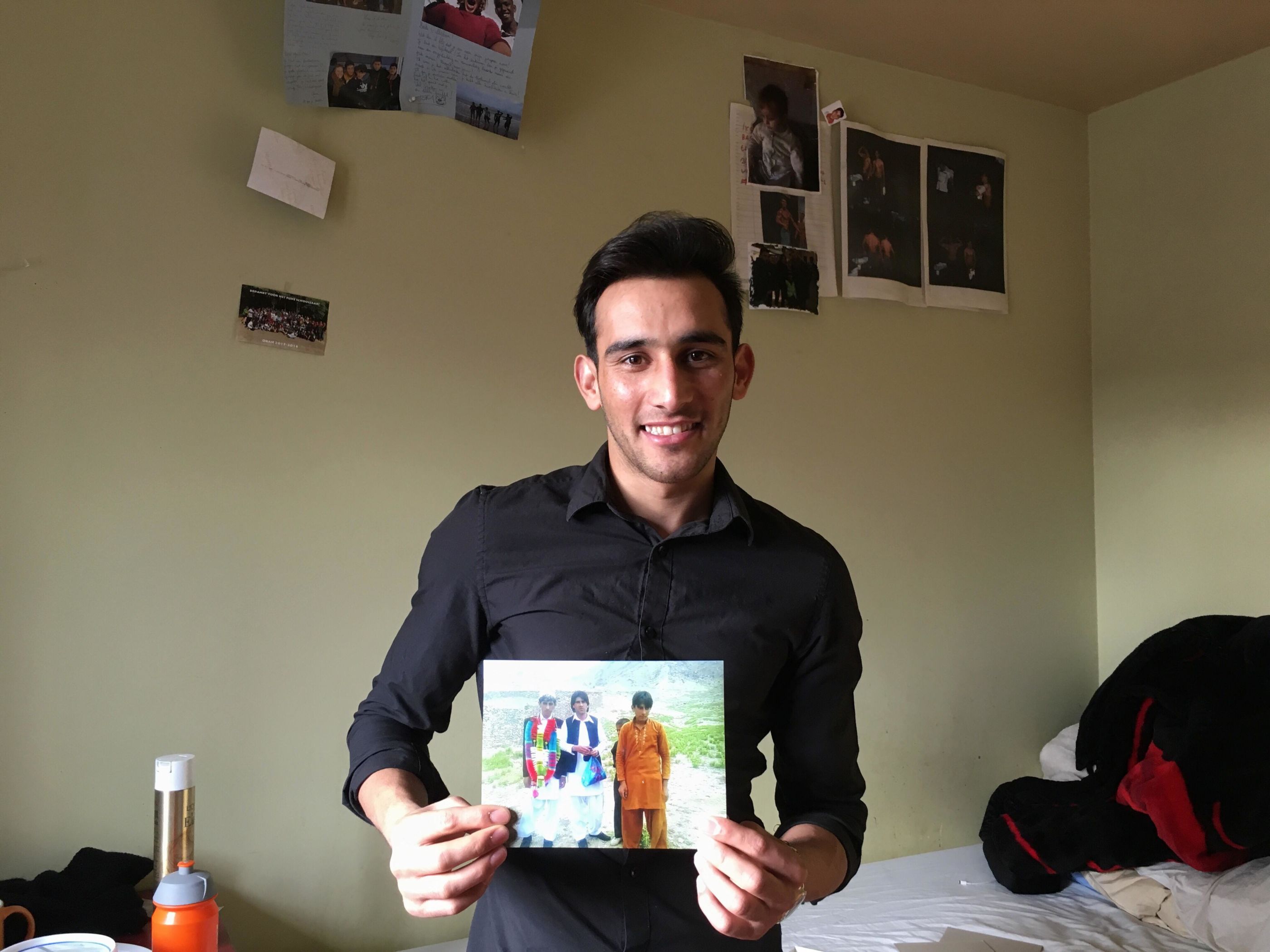 © Elise Schroons - Malistan in zijn kamer in Gent. Hier toont hij een foto van zichzelf (oranje gewaad), een neef en een vriend van hem in Afghanistan. Nu is hij 17 jaar. 